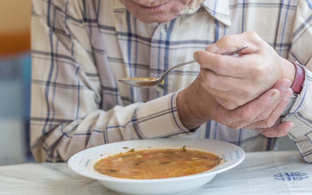 homem idoso com dificuldades em alimentar-se devido aos problemas resultantes da Doença de Parkinson