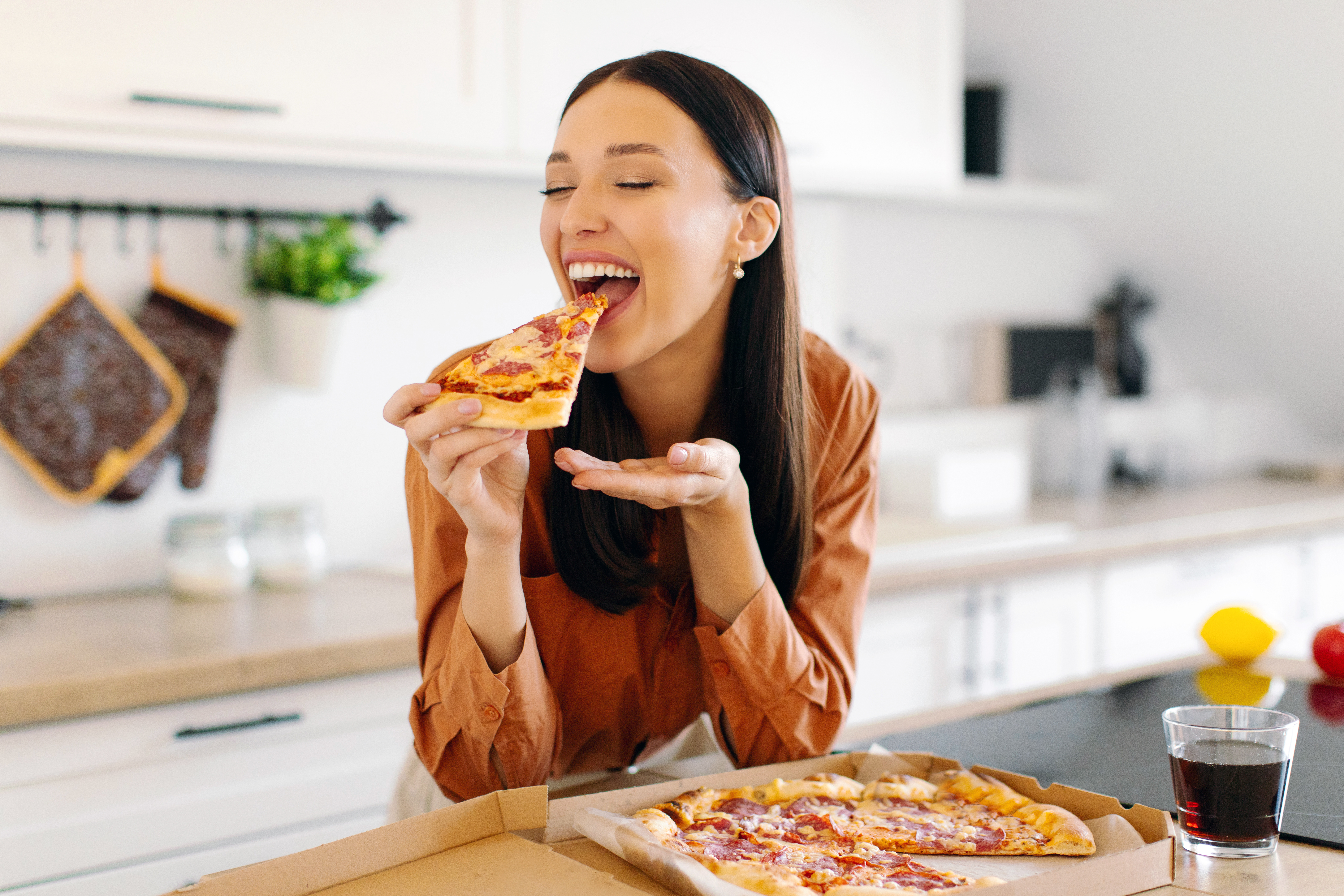 Mulher a comer pizza, exemplo de alimento rico em gorduras associado à dislipidemia