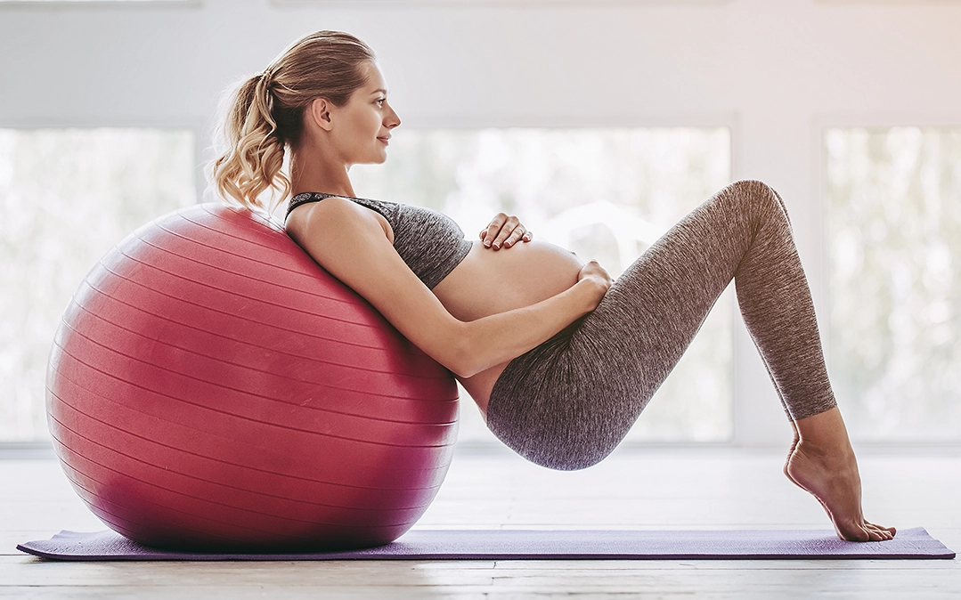 mulher grávida a fazer exercício físico com uma bola grande de Pilates