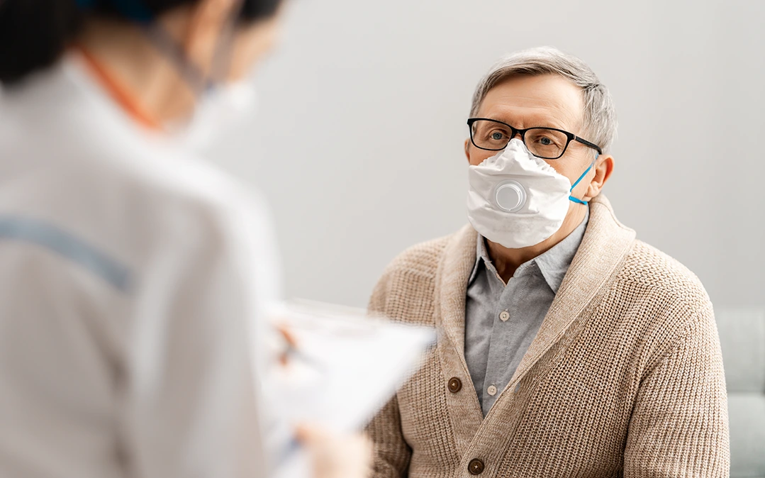 homem a utilizar uma máscara em uma consulta pós-covid a responder questões postas pela enfermeira 