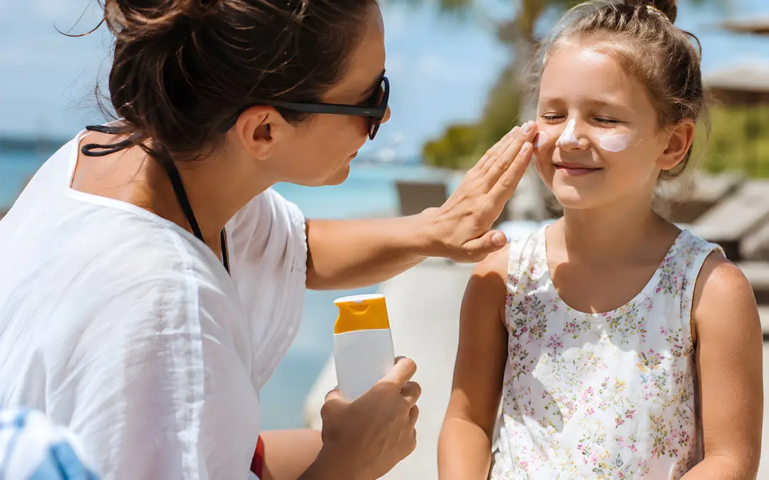 mãe passa protetor solar na filha na praia durante as férias de verão para a proteger dos raios uv do sol 