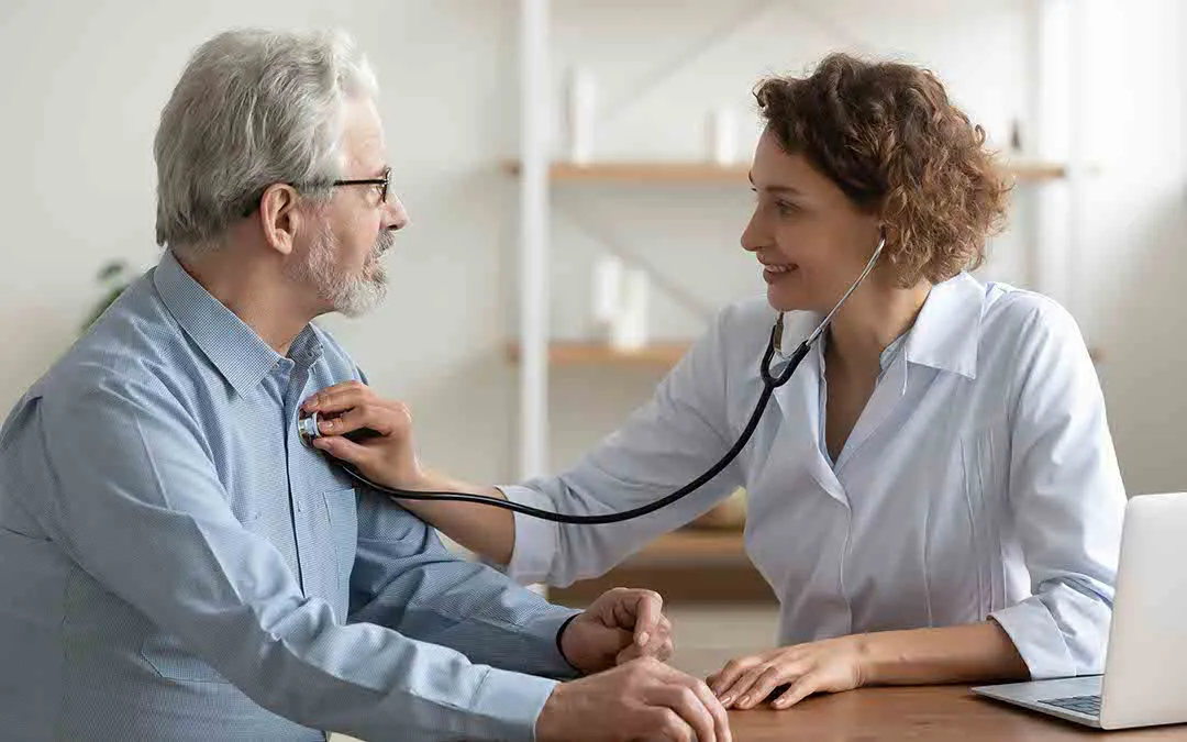 um homem idoso em uma consulta médica com uma doutora a utilizar um estetoscópio para escutar os batimentos cardíacos do utente 