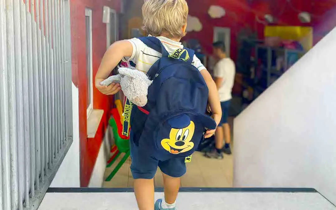 um menino com roupas de escola e uma mochila a entrar na escola