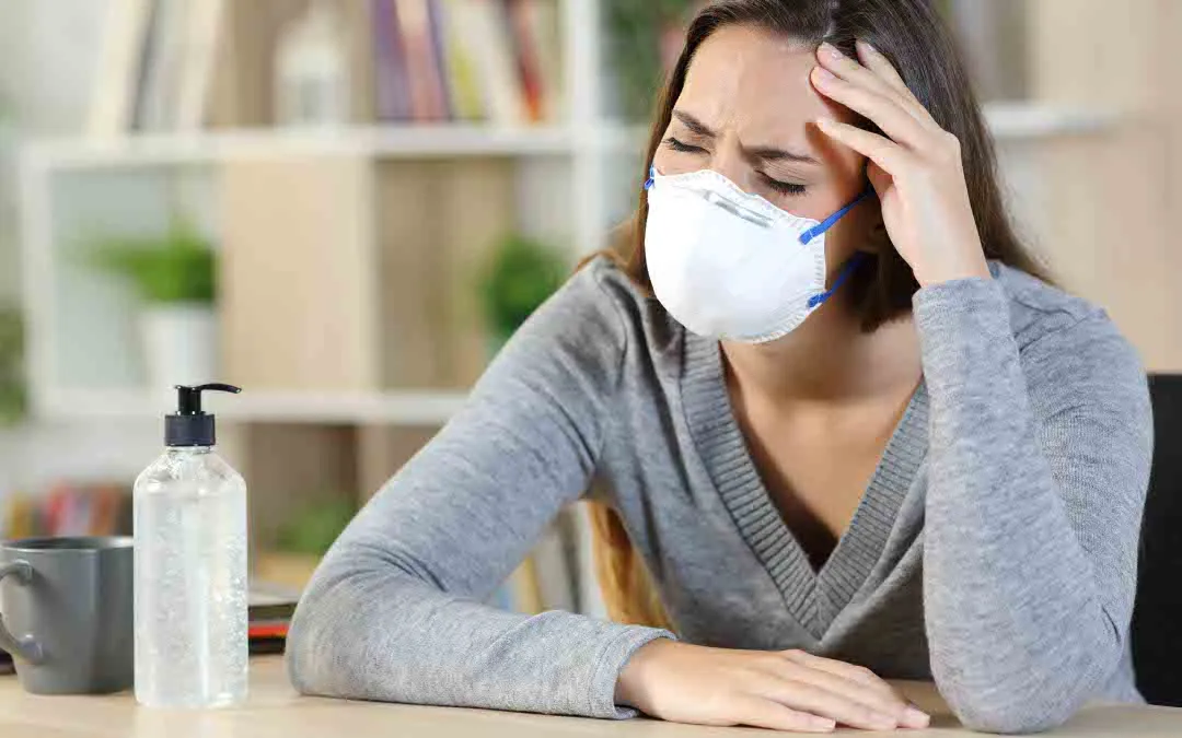 Mulher com máscara a sentir sintomas como dor de cabeça e cansaço