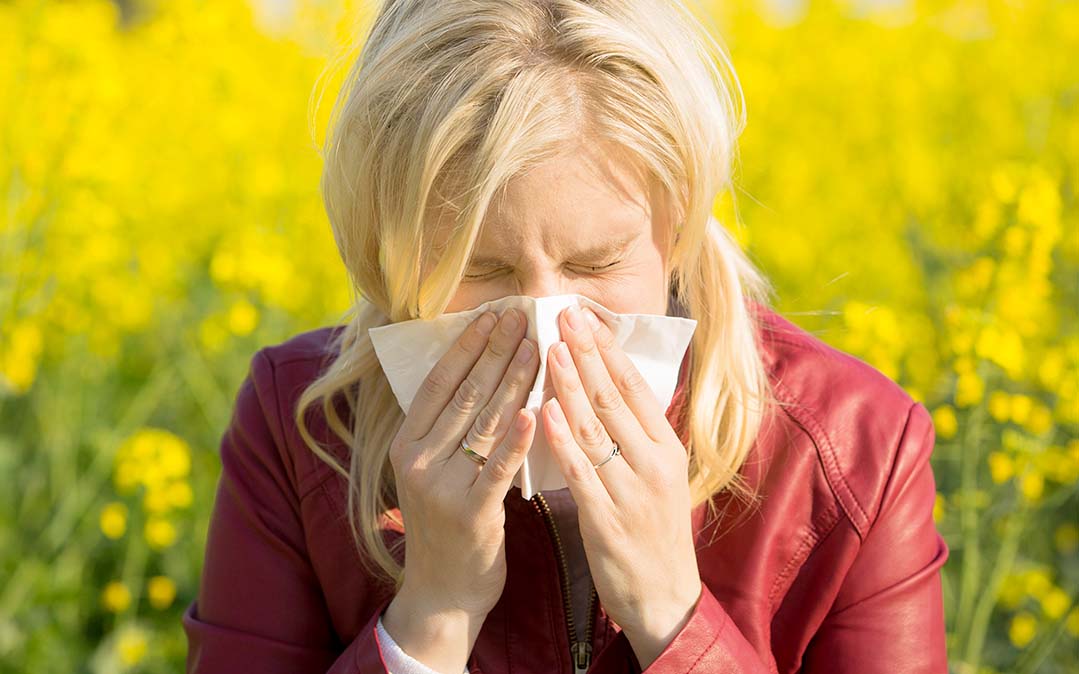 mulher, no campo e rodeada de flores, espirra para um lenço branco
