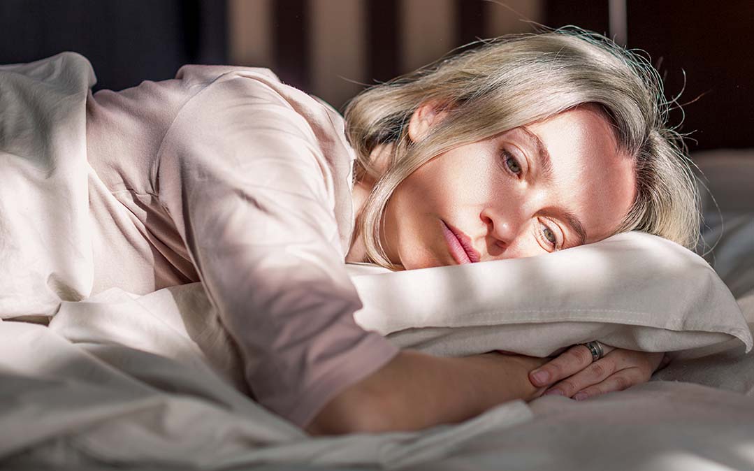 mulher com semblante triste está deitada na cama, sugerindo estar sozinha
