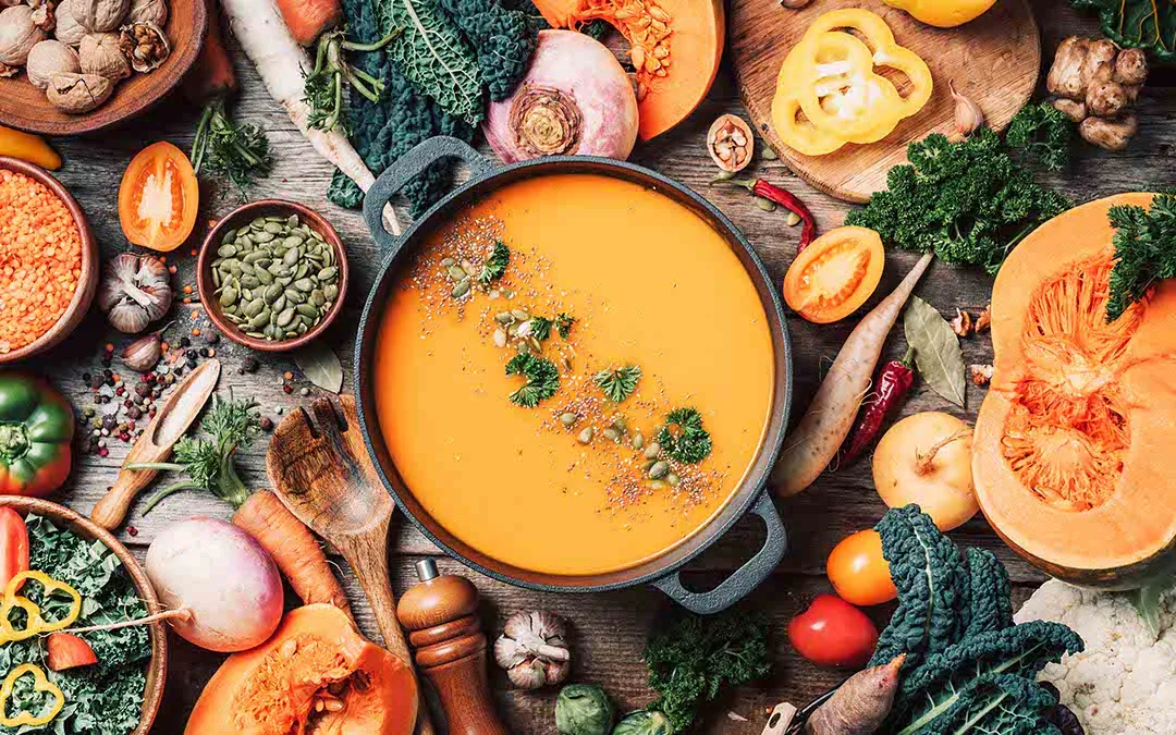 Sopa cremosa de abóbora rodeada de legumes frescos e sementes – receita saudável e nutritiva